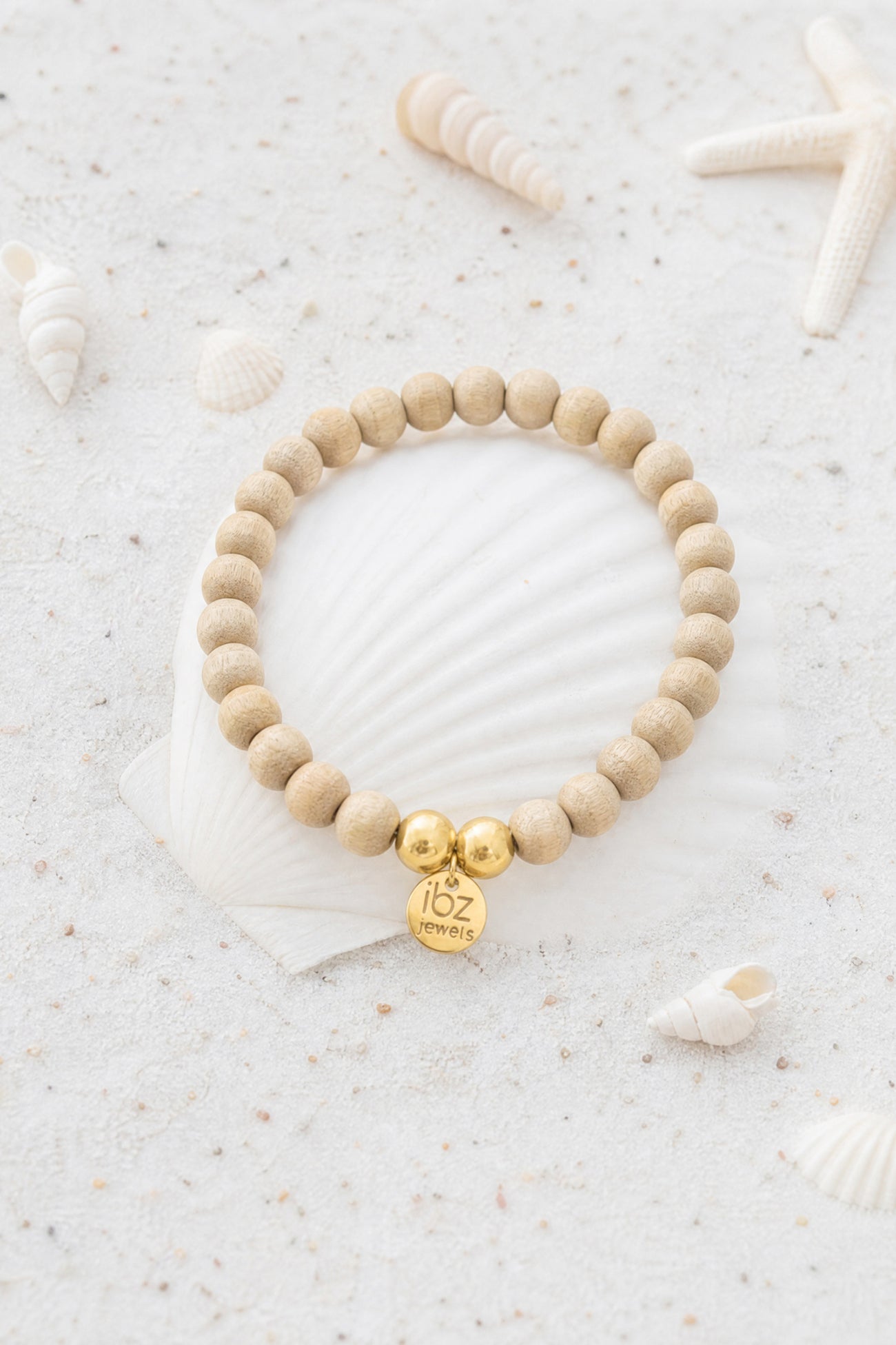 Ibzjewels Bracelet Arcana Gold with natural wooden beads, white beads and gold plated charm on a beach-inspired background.