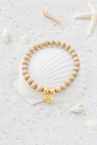 Ibzjewels Bracelet Arcana Gold with natural wooden beads, white beads and gold plated charm on a beach-inspired background.